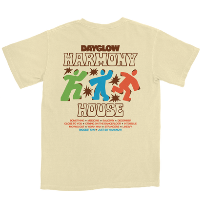 A cream-colored t-shirt featuring a retro-style graphic print of the Dayglow 'Harmony House' logo with colorful figures and text, displayed on a solid white background.